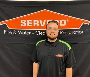 A tall man smiling with brown/red hair and a beard. Wearing a black SERVPRO shirt