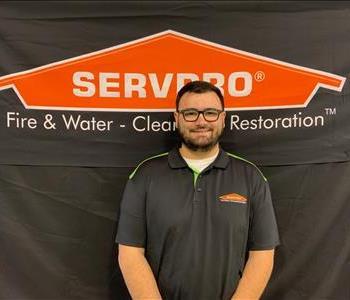 A man with glasses. He has dark hair and  a beard. He is wearing a black SERVPRO shirt